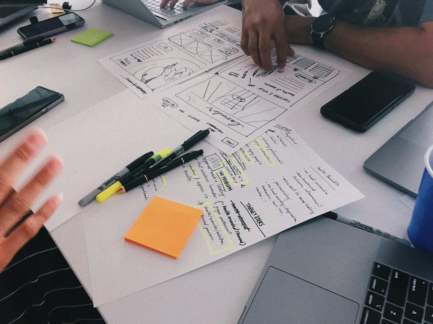 Three people collaborate on strategy documents and laptops at a white table.